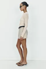 Falda pantalón corta de tiro medio en color beige, con bolsillos delanteros y cierre frontal de cremallera. Incluye un cinturón negro integrado con hebilla metálica redonda.