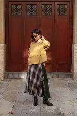 Falda midi de diseño asimétrico que combina un panel de tela escocesa en tonos verdes, blancos y marrones con un panel lateral de paño verde oscuro. Presenta un tajo lateral pronunciado y tiro a la cintura.