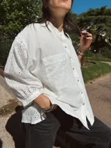 Camisa blanca de broderie y tusor, corte holgado, con cuello mao, mangas largas abullonadas con puños elásticos, cierre frontal con botones y bolsillo de parche en el pecho.
