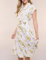 Vestido camisero midi de silueta evasé, confeccionado en tejido liviano blanco con estampado floral amarillo y rayas celestes. Cuenta con cuello solapa en V, cartera con botones frontales, mangas cortas japonesas y cintura definida con lazo ajustable a juego.
