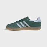 Championes Adidas Gazelle Indoor de gamuza verde oscuro, con las tres tiras características en color blanco y el nombre del modelo en letras doradas en el lateral. Poseen suela de goma translúcida y detalles en color celeste claro en el talón.