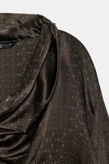 Blusa de seda color marrón oscuro con estampado geométrico sutil. Presenta un diseño de cuello fluido tipo pañuelo, manga larga con puños anchos y una caída suave y elegante.