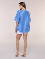 Blusa de corte cuadrado y silueta amplia, color azul con diseño de rayas verticales en tonos más claros. Cuenta con cuello redondo y mangas cortas acampanadas, decoradas con una hilera de botones de madera sobre los hombros.