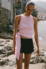Top halter entallado de popelina color rosado, con diseño de pliegues en diagonal y lazo ajustable en el bajo. Cuenta con cierre lateral con cremallera oculta en la costura.