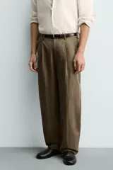 Pantalón de corte relajado confeccionado en mezcla de algodón y lino, con diseño de pliegues frontales, bolsillos laterales y bolsillos traseros de vivo. Presenta cierre frontal con cremallera y botón, con un acabado de lavado especial que le otorga una apariencia única.
