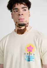 Remera color crema de algodón con estampa en el pecho de una flor rosa sobre una torre de transmisión y el logo de Obey.