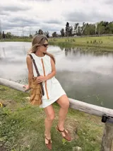 Vestido corto de jean crudo, de silueta holgada y sin mangas, con una tira vertical central de cuero color camel y bolsillos laterales.