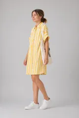 Vestido camisero corto de silueta relajada, con estampado de rayas verticales en color amarillo y blanco. Presenta cuello clásico, cierre frontal con botones y mangas cortas.