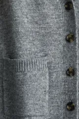Cárdigan de punto gris jaspeado, con cuello en V, botones frontales y dos bolsillos delanteros abiertos. Presenta un corte holgado y hombros caídos, con puños y bajo acanalados.