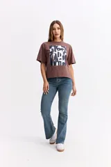 Remera de algodón color marrón con estampa gráfica frontal en tonos oscuros y texto.