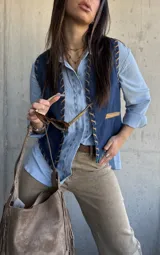 Chaleco de denim azul oscuro con detalles de costuras decorativas y ribetes en tono tostado.