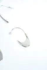 Set de tres pares de aros plateados de diseño variado, incluyendo aros de argolla texturados, aros colgantes alargados y aros con dijes en forma de medialuna.