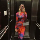 Vestido midi ajustado con estampado abstracto en tonos naranja, rosa y azul. Tiene cuello alto y mangas largas.
