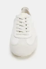 Zapatilla deportiva color blanco con detalles en gamuza y diseño de talonera elástica, cordones al tono y suela plana dentada.
