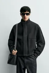 Cazadora de corte boxy fit en tejido acanalado con interior polar. Presenta cuello subido, manga larga con puños, bolsillos frontales tipo canguro y cierre frontal de cremallera oculta por solapa con botones a presión.