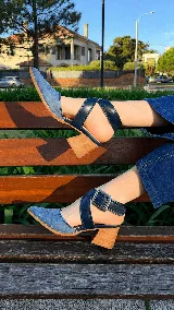 Zapatos de tacón ancho color camel con textura símil serpiente, punta fina y tiras cruzadas con hebilla metálica grande en el lateral.
