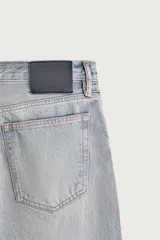 Pantalón denim de corte recto desde la cadera hasta el tobillo, de tiro medio y color celeste claro con efecto lavado. Cuenta con diseño clásico de cinco bolsillos y cierre frontal con cremallera y botón metálico.