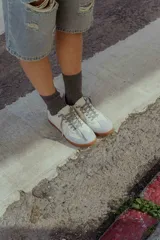 Zapatillas urbanas de cuero color crema con puntera y talón en gamuza gris, suela de goma marrón y cordones grises.