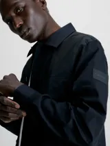 Camisa negra de popelina con corte relaxed, cierre frontal con botones, mangas largas y dos bolsillos con solapa en el pecho.