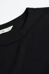 Remera negra de manga larga, confeccionada en punto acanalado suave de mezcla de algodón, con cuello redondo.