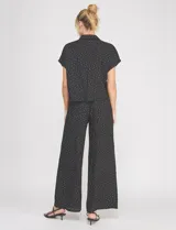 Blusa crop cruzada Allie Rose de tela liviana negra con estampado de lunares blancos, escote en V y cuello camisero.