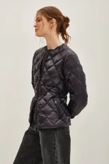 Campera acolchada de diseño matelassé con cierre frontal y cinturón ajustable con hebilla metálica. Presenta cuello redondo y mangas largas con puños elásticos.