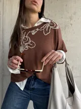 Sweater de punto color chocolate, de corte holgado, manga larga y cuello redondo con delicados bordados contrastantes en el frente.