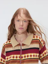 Campera de punto estampada de corte holgado, con cierre metálico frontal y cuello de corderito sintético en color tostado. Presenta un diseño de franjas horizontales con patrones geométricos en tonos bordó, mostaza, marrón y beige.