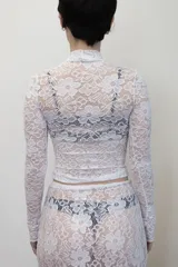 Remera negra de manga larga confeccionada en encaje, con cuello redondo y corte ajustado al cuerpo.