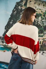 Cardigan oversized de punto grueso, color azul marino y blanco con franjas rojas y rosadas en el cuello, puños y solapa. Tiene botones grandes marrones y el logo de Anthea bordado en el pecho.