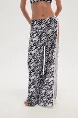 Pantalon de corte ancho y tiro bajo, con aberturas laterales pronunciadas y ribete blanco en los bordes. Presenta un estampado abstracto en tonos blanco y negro.