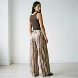 Pantalón de corte ancho y tiro alto con estampado de piel de serpiente en tonos beige y marrón. Presenta diseño de cinco bolsillos y cierre frontal con botón y cremallera.