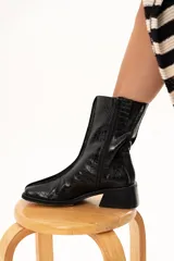 Bota de caña media color negro con textura de reptil, confeccionada en cuero. Presenta horma cuadrada, cierre lateral interno, taco cuadrado y una pequeña plataforma.