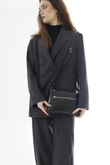 Bandolera de cuero negro, de diseño rectangular y compacto, con correa ajustable para llevar cruzada al hombro. Cuenta con un bolsillo frontal con cierre y detalles de costuras pespuntadas a contratono.