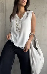 Blusa blanca sin mangas con cuello en V y detalle de puntilla en el ruedo. Cierre con botones.