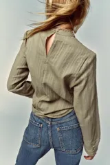 Camisa verde claro con cuello alto de puntilla, manga larga y detalles de entredoses calados en el pecho y los hombros. Cierre en la espalda con abertura y botón oculto.