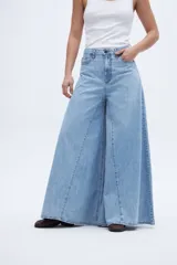 Jean de mezclilla celeste claro, tiro medio, con corte extremadamente ancho y acampanado desde la cadera hasta el bajo, con costuras verticales que acentúan la amplitud de la pierna.