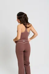 Conjunto deportivo compuesto por un top de escote redondo con breteles anchos y una calza larga de tiro alto. Ambas prendas son de color marrón con detalles de costuras blancas a contratono y el logo bk. estampado en el frente del top.