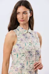 Camisa sin mangas de lino y algodón, con estampado floral en tonos violeta y verde sobre base beige, cuello camisero y cierre frontal de botones.