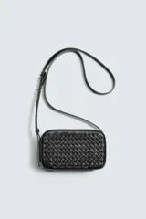 Bandolera pequeña de color negro con cuerpo rectangular y textura trenzada en el frente. Posee un asa de hombro ajustable y extraíble.