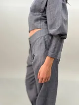 Pantalón de vestir gris con bolsillos laterales, pretina a la cintura y tablas en los bajos.