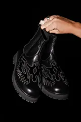 Bota tipo chelsea de cuero negro con suela track y diseño de águila bordado en hilo blanco en la parte frontal.