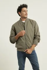 Campera tipo bomber color verde militar, confeccionada en 100% algodón. Cuenta con puños tejidos al tono, cuello y cintura elásticos, y cierre frontal metálico.