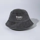 Gorro tipo bucket gris con efecto gastado, confeccionado en gabardina y con bordado frontal en hilo blanco con la inscripción "Inspire GREATNESS by vcp".
