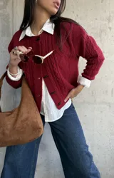 Cardigan de punto con textura trenzada en color bordó, con cuello redondo y cierre frontal mediante botones tipo alamar. Presenta mangas largas con puños acanalados y un corte clásico.