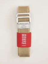 Cinto de lona color beige con hebilla metálica de diseño rectangular doble y detalle de marca grabada.