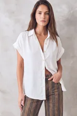 Blusa blanca de manga corta con cuello camisero y cierre frontal de botones, confeccionada en tejido de poliéster suave y fluido con diseño holgado.
