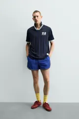 Polo de corte relajado confeccionado en tejido técnico, con diseño de rayas verticales en tonos azul marino y negro. Presenta cuello solapa con abertura frontal y detalles de rib en contraste en cuello y mangas. Incluye estampado frontal con el número 98 y la inscripción France, además de una etiqueta aplicada en el ruedo inferior.