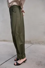 Pantalón de tiro alto en color verde militar, con corte barrel de pernera holgada que se estrecha hacia el tobillo. Presenta trabillas laterales ajustables en la cintura y en el bajo, bolsillos delanteros y cierre frontal con cremallera y botón.