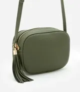 Cartera bandolera pequeña de diseño rectangular, confeccionada en poliuretano color verde oliva. Presenta cierre superior con cremallera y detalle de borla decorativa en el lateral, con correa larga ajustable.